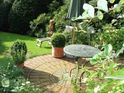 Kleiner runder Sitzplatz aus Klinker-pflaster und Granit-steinen in einem formalen Garten.